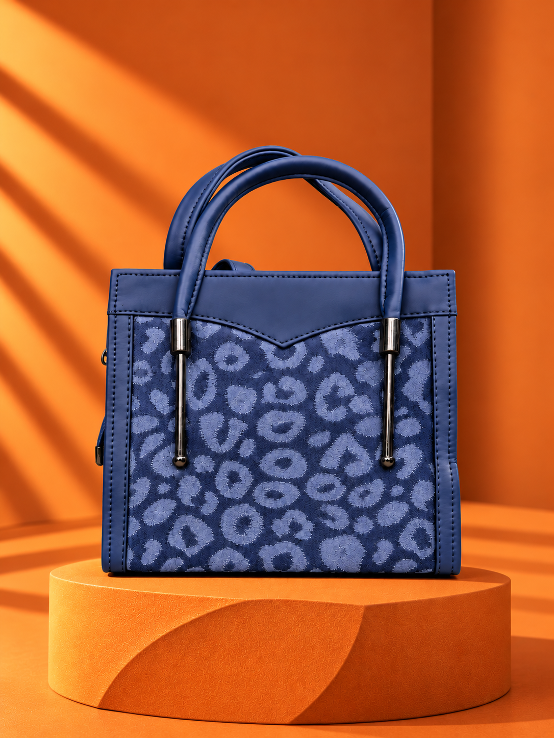 Ramlah blue patterned tote bag for women with double handles and metallic detailing on an orange studio pedestal.